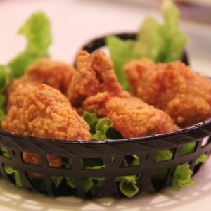 Close-up of crispy fried chicken served in a black basket with fresh lettuce, highlighting food texture.