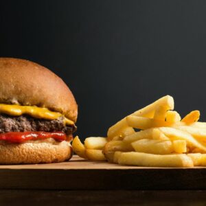 Appetizing burger with meat patty ketchup and cheese placed on wooden table with crispy french fries against black background