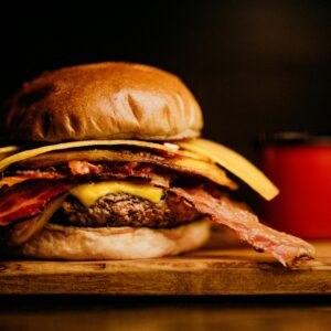 Close-up of a gourmet bacon cheeseburger with a side of crispy fries on a wooden board.